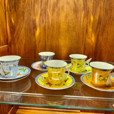 Sale Photo Thumbnail #53: Set of five porcelain espresso cups and saucers featuring colorful butterfly motifs and wing-shaped handles, displayed inside a wooden cabinet.