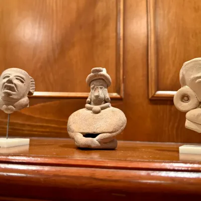 Sale Photo Thumbnail #58: Trio of Pre-Columbian style terracotta head and figure fragments displayed on individual stands and a wooden surface.