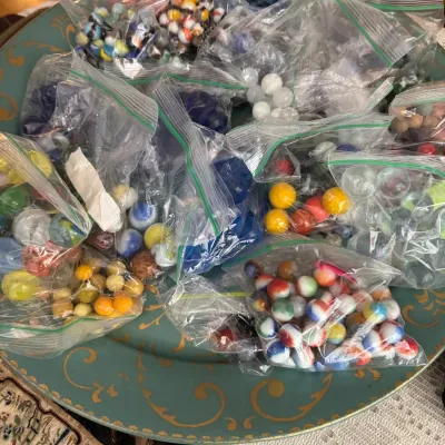 Sale Photo Thumbnail #82: Assortment of colorful glass marbles sorted into individual plastic ziplock bags, displayed on a green decorative tray.