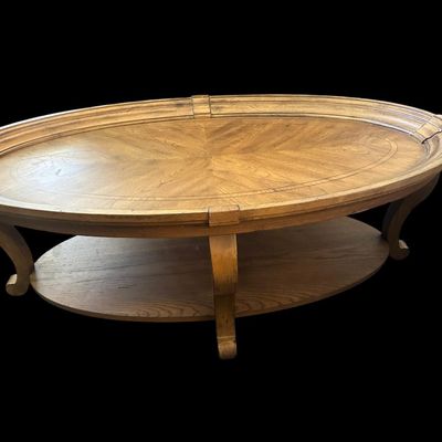 Sale Photo Thumbnail #161: 52"L × 30"W × 18"T. Hidden casters. Beautiful oval coffee table featuring starburst oak veneer wood inlay top  molded picture-frame gallery edge  cabriole legs  and lower oval wood display shelf. Hidden casters mounted on underside for easy moving. Dime