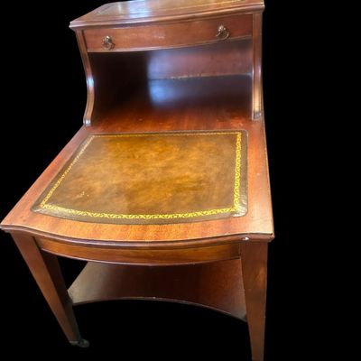 Sale Photo Thumbnail #960: 24.00 x 19.00 x 26.00 Classic 2-tier step-down end table featuring gold-tooled leather inlays on both upper and lower surface tiers  top drawer with brass ring pulls  and lower curved open shelf base.  