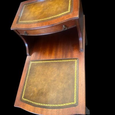 Sale Photo Thumbnail #962: 24.00 x 19.00 x 26.00 Classic 2-tier step-down end table featuring gold-tooled leather inlays on both upper and lower surface tiers  top drawer with brass ring pulls  and lower curved open shelf base.  
