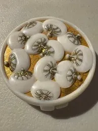 Vintage round compact featuring a decorative lid with white, dome-shaped elements and gold-tone accents.