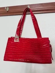 Bright red patent leather shoulder bag with a textured faux-croc pattern and silver-tone hardware, hanging from a wall hook.