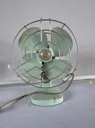 Vintage mid-century electric desk fan in a pale mint green finish with a wire safety cage.