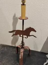 Rustic metal table lamp featuring a running horse silhouette, designed in a weathervane style with a tripod base.