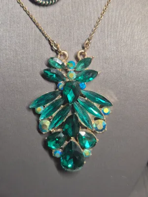 Sale Photo Thumbnail #117: A vintage costume jewelry set featuring a gold-tone chain necklace with a large, tiered pendant set with emerald green marquise and teardrop rhinestones, accented by iridescent aurora borealis rhinestones. Accompanied by a matching pair of gold-tone dangl
