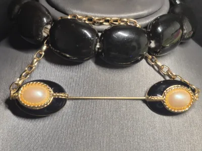 Sale Photo Thumbnail #197: A vintage costume jewelry set featuring a matching pair of clip-on earrings, a beaded stretch bracelet, and a bar pin. The pieces are designed with black oval elements, gold-tone rope borders, and central faux pearl cabochons. The set shows some light wea