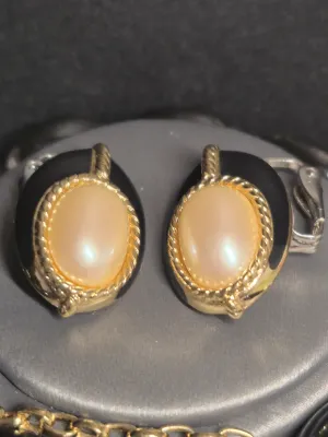 Sale Photo Thumbnail #199: A vintage costume jewelry set featuring a matching pair of clip-on earrings, a beaded stretch bracelet, and a bar pin. The pieces are designed with black oval elements, gold-tone rope borders, and central faux pearl cabochons. The set shows some light wea