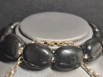 Sale Photo Thumbnail #198: A vintage costume jewelry set featuring a matching pair of clip-on earrings, a beaded stretch bracelet, and a bar pin. The pieces are designed with black oval elements, gold-tone rope borders, and central faux pearl cabochons. The set shows some light wea