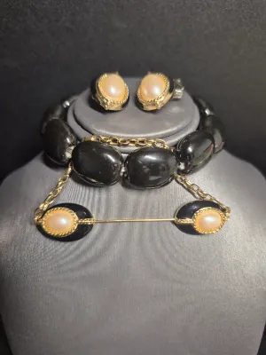 Sale Photo Thumbnail #196: A vintage costume jewelry set featuring a matching pair of clip-on earrings, a beaded stretch bracelet, and a bar pin. The pieces are designed with black oval elements, gold-tone rope borders, and central faux pearl cabochons. The set shows some light wea