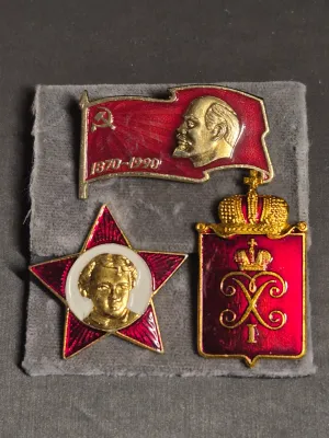 Sale Photo Thumbnail #261: A collection of three vintage Soviet-era Russian enamel pin badges. Includes a red star Little Octoberist badge featuring a young Vladimir Lenin, a red flag commemorative badge marked '1870-1990' with Lenin's profile, and a Peterhof 1705 imperial-style sh