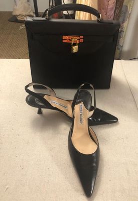 REINA of Italy black leather top-handle Kelly handbag with gold-tone hardware and padlock, paired with black leather Manolo Blahnik...