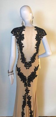 Elegant floor-length evening gown in a nude tone, featuring intricate black lace applique detailing along the back and shoulders....