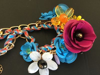 Sale Photo Thumbnail #13: Vibrant costume statement bib necklace featuring multi-colored molded flower motifs in magenta, blue, white, yellow, and amber. The flowers are arranged along a gold-tone chain interwoven with a red, blue, and white patterned cord. Features adjustable cha