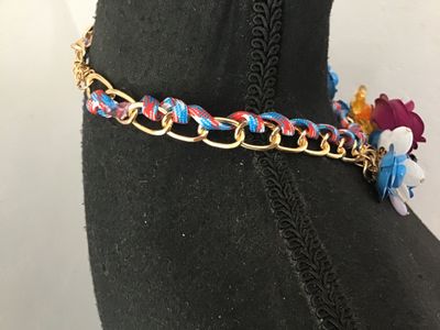 Sale Photo Thumbnail #12: Vibrant costume statement bib necklace featuring multi-colored molded flower motifs in magenta, blue, white, yellow, and amber. The flowers are arranged along a gold-tone chain interwoven with a red, blue, and white patterned cord. Features adjustable cha
