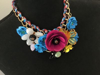 Sale Photo Thumbnail #14: Vibrant costume statement bib necklace featuring multi-colored molded flower motifs in magenta, blue, white, yellow, and amber. The flowers are arranged along a gold-tone chain interwoven with a red, blue, and white patterned cord. Features adjustable cha