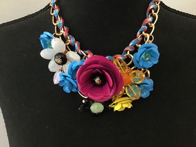 Sale Photo Thumbnail #11: Vibrant costume statement bib necklace featuring multi-colored molded flower motifs in magenta, blue, white, yellow, and amber. The flowers are arranged along a gold-tone chain interwoven with a red, blue, and white patterned cord. Features adjustable cha