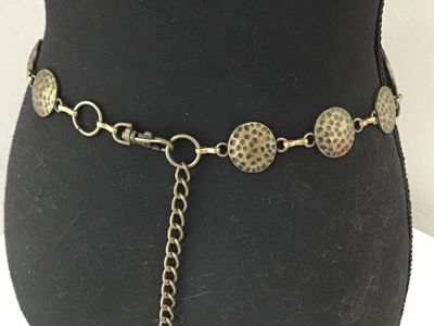 Sale Photo Thumbnail #21: Boho style chain belt featuring linked, hammered circular metal discs in a antique brass/bronze tone finish. Includes an adjustable tail chain with a clasp closure. Shows light vintage wear consistent with age, overall good condition.