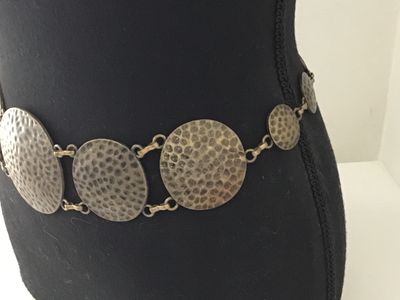 Sale Photo Thumbnail #19: Boho style chain belt featuring linked, hammered circular metal discs in a antique brass/bronze tone finish. Includes an adjustable tail chain with a clasp closure. Shows light vintage wear consistent with age, overall good condition.