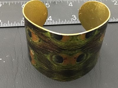 Sale Photo Thumbnail #38: A wide metal cuff bracelet featuring a vivid glossy peacock feather pattern on the exterior with a gold-tone brass interior finish. Measures approximately 1.75 to 2 inches wide. Shows minor wear along the edges and interior surface, but overall in good, w