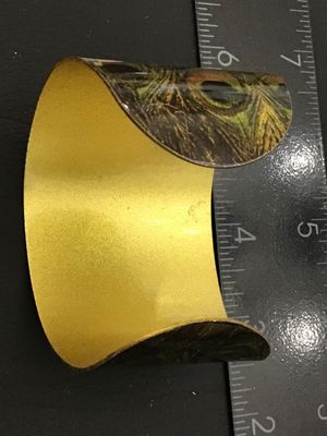 Sale Photo Thumbnail #40: A wide metal cuff bracelet featuring a vivid glossy peacock feather pattern on the exterior with a gold-tone brass interior finish. Measures approximately 1.75 to 2 inches wide. Shows minor wear along the edges and interior surface, but overall in good, w