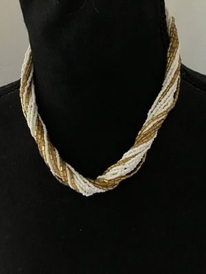 Sale Photo Thumbnail #44: Multi-strand twisted torsade necklace featuring alternating strands of white seed beads and metallic gold-tone glass bugle beads. It features decorative white molded end caps and a gold-tone push-in box clasp with a sunburst pattern. In good vintage condi