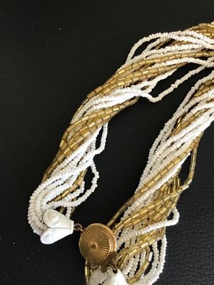 Sale Photo Thumbnail #46: Multi-strand twisted torsade necklace featuring alternating strands of white seed beads and metallic gold-tone glass bugle beads. It features decorative white molded end caps and a gold-tone push-in box clasp with a sunburst pattern. In good vintage condi