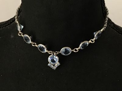 Sale Photo Thumbnail #63: Vintage silver-tone choker necklace featuring bezel-set round light blue glass rhinestones and a central drop pendant with additional small rhinestone accents. Measures approximately 14-15 inches in length. Secured with a fold-over clasp. Good vintage con