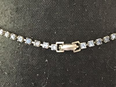 Sale Photo Thumbnail #64: Vintage silver-tone choker necklace featuring bezel-set round light blue glass rhinestones and a central drop pendant with additional small rhinestone accents. Measures approximately 14-15 inches in length. Secured with a fold-over clasp. Good vintage con
