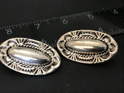 Sale Photo Thumbnail #66: Pair of oval silver-tone clip-on earrings featuring Southwestern style stamped detailed borders, rope trim accents, and raised central domes. Each earring measures approximately 1.25 inches in length. Clip backs are intact and functional. Excellent pre-ow