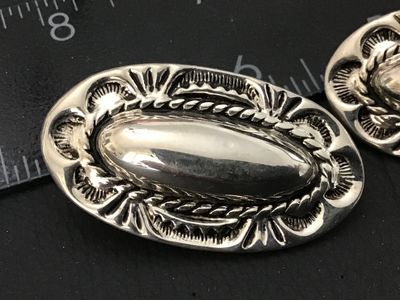 Sale Photo Thumbnail #65: Pair of oval silver-tone clip-on earrings featuring Southwestern style stamped detailed borders, rope trim accents, and raised central domes. Each earring measures approximately 1.25 inches in length. Clip backs are intact and functional. Excellent pre-ow