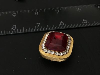 Sale Photo Thumbnail #69: Vintage gold-tone brooch featuring a large, emerald-cut red glass/rhinestone center stone surrounded by a halo of clear pave rhinestones. Textured brushed gold-tone finish with pin back mechanism and hook attachment. Measures approximately 1.5 inches wide