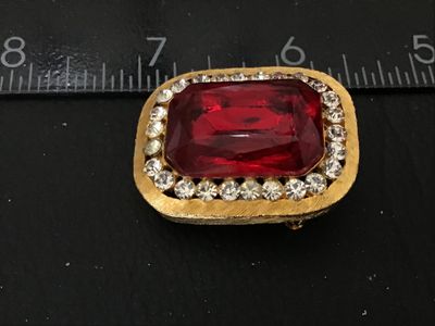 Sale Photo Thumbnail #68: Vintage gold-tone brooch featuring a large, emerald-cut red glass/rhinestone center stone surrounded by a halo of clear pave rhinestones. Textured brushed gold-tone finish with pin back mechanism and hook attachment. Measures approximately 1.5 inches wide