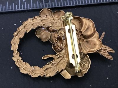 Sale Photo Thumbnail #84: A vintage gold-tone metal brooch featuring a wreath design adorned with sculpted flowers, leaves, and a dragonfly detail. Accentuated with aurora borealis (AB) iridescence rhinestones. Standard pin-back closure in working order. Measures approximately 2 i