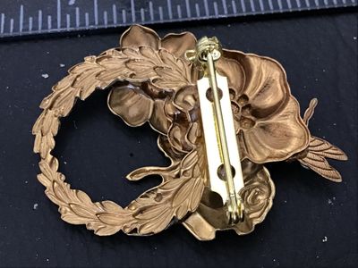 Sale Photo Thumbnail #83: A vintage gold-tone metal brooch featuring a wreath design adorned with sculpted flowers, leaves, and a dragonfly detail. Accentuated with aurora borealis (AB) iridescence rhinestones. Standard pin-back closure in working order. Measures approximately 2 i