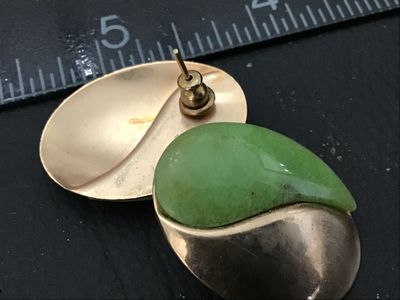 Sale Photo Thumbnail #85: Pair of vintage oval-shaped pierced post earrings featuring a swirl design half smooth gold-tone metal and half light green stone or jadeite inlay. Each earring measures approximately 1 inch in length. Good vintage condition with minor surface wear visibl