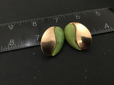 Sale Photo Thumbnail #86: Pair of vintage oval-shaped pierced post earrings featuring a swirl design half smooth gold-tone metal and half light green stone or jadeite inlay. Each earring measures approximately 1 inch in length. Good vintage condition with minor surface wear visibl