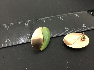 Sale Photo Thumbnail #87: Pair of vintage oval-shaped pierced post earrings featuring a swirl design half smooth gold-tone metal and half light green stone or jadeite inlay. Each earring measures approximately 1 inch in length. Good vintage condition with minor surface wear visibl