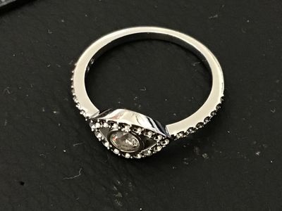 Sale Photo Thumbnail #96: Silver-tone band ring featuring a central evil eye design set with clear round crystals and crystal accents along the shoulders. Inside band exhibits maker's hallmarks. Measured on ring mandrel as approximately size 6. Pre-owned condition with light wear.