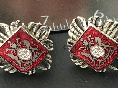 Sale Photo Thumbnail #99: Pair of vintage clip-on earrings featuring a textured silver-tone crown motif surrounding a diamond-shaped red enamel panel. The central shield showcases a detailed coat of arms/heraldic crest design. Silver-tone textured backs with functional clip closur