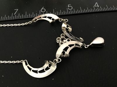 Sale Photo Thumbnail #108: A vintage silver-tone festoon style necklace featuring filigree-style openwork links, accented with clear round and marquise-cut rhinestones and a dangling teardrop rhinestone centerpiece. The center feature measures approximately 3 inches across, and the