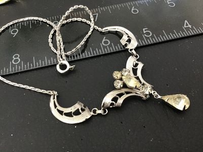 Sale Photo Thumbnail #110: A vintage silver-tone festoon style necklace featuring filigree-style openwork links, accented with clear round and marquise-cut rhinestones and a dangling teardrop rhinestone centerpiece. The center feature measures approximately 3 inches across, and the