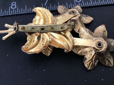 Sale Photo Thumbnail #116: Vintage gold-tone brooch featuring a floral bouquet design set with colorful round rhinestones in red, aqua blue, and amber yellow. The back features a standard pin bar closure. Measures approximately 3 inches in length. Shows vintage wear including patin