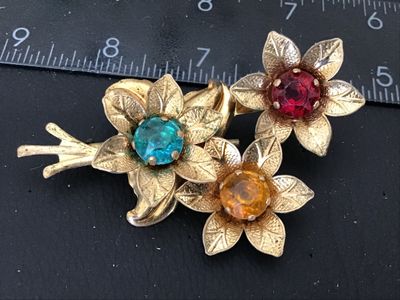 Sale Photo Thumbnail #114: Vintage gold-tone brooch featuring a floral bouquet design set with colorful round rhinestones in red, aqua blue, and amber yellow. The back features a standard pin bar closure. Measures approximately 3 inches in length. Shows vintage wear including patin