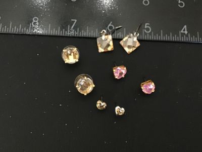 Sale Photo Thumbnail #118: Lot of 5 pairs of fashion earrings including:
- Juicy Couture heart-shaped logo studs (gold-tone and silver-tone style)
- Pink heart-shaped faceted crystal studs with gold-tone prong settings
- Champagne round faceted crystal studs with disc backs
- Champ