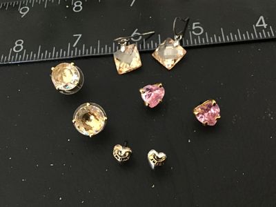Sale Photo Thumbnail #119: Lot of 5 pairs of fashion earrings including:
- Juicy Couture heart-shaped logo studs (gold-tone and silver-tone style)
- Pink heart-shaped faceted crystal studs with gold-tone prong settings
- Champagne round faceted crystal studs with disc backs
- Champ