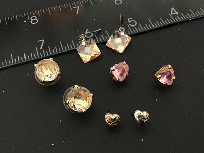 Sale Photo Thumbnail #120: Lot of 5 pairs of fashion earrings including:
- Juicy Couture heart-shaped logo studs (gold-tone and silver-tone style)
- Pink heart-shaped faceted crystal studs with gold-tone prong settings
- Champagne round faceted crystal studs with disc backs
- Champ