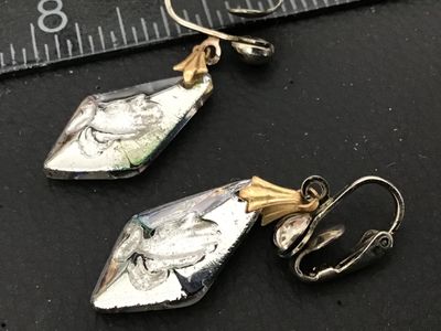 Sale Photo Thumbnail #126: Pair of vintage clip-on dangle earrings featuring iridescent aurora borealis (AB) glass or crystal drop pendants. Each crystal is diamond-shaped with an Intaglio-style molded or etched praying hands design highlighted in white on the front and silver foil