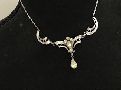 Sale Photo Thumbnail #131: Small lot of vintage items including an advertising lapel pin featuring Reddy Kilowatt, marked on the back with REDDY KILOWATT and a registered trademark symbol, measuring under 1 inch tall. Also includes a silver-tone filigree necklace featuring clear rh